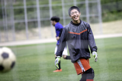 サッカーグラウンドで笑顔を見せるゴールキーパーの高校生アスリート